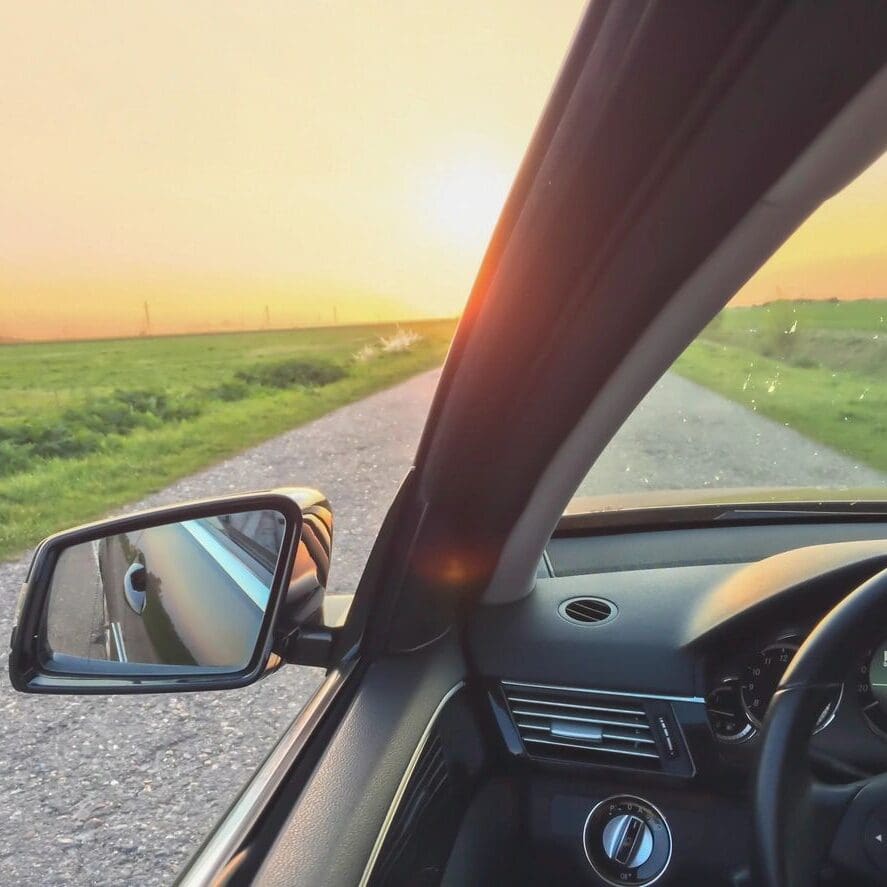 A car driving down the road with a sunset in the background.